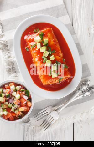Burrito umido farcito con carne grattugiata, fagioli, riso e formaggio, affumicato in salsa di enchilada rossa sul piatto della tavola di legno. Verticale a. Foto Stock