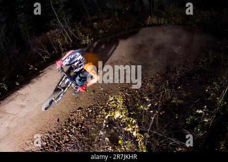 Maschio mountain bike su pista singola. Manovra di una svolta brusca su un sentiero sterrato. Casco, guanti e foglie di caduta sul sentiero. Foto Stock