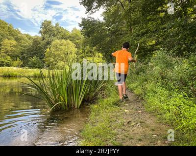 Ragazzo a piedi lungo il sentiero con canna da pesca vicino al lago. Foto Stock