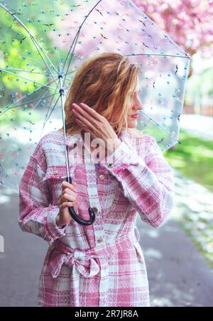 Donna che tiene un ombrello alla moda nel parco in primavera durante la passeggiata Foto Stock