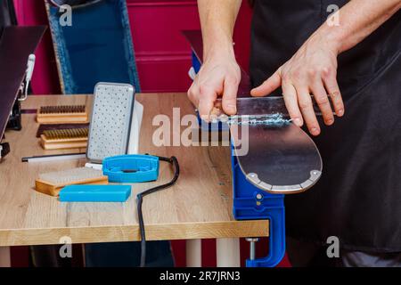 Le mani rimuovono la cera in eccesso dalla base dello sci con un raschietto sul banco di lavoro Foto Stock