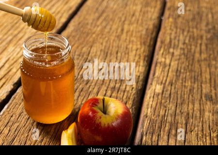 Vista dall'alto del cucchiaio di miele sopra il vaso di miele e la mela su un tavolo di legno, spazio per copia Foto Stock
