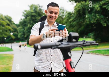 Uomo sorridente che noleggia scooter elettrico al parco Foto Stock