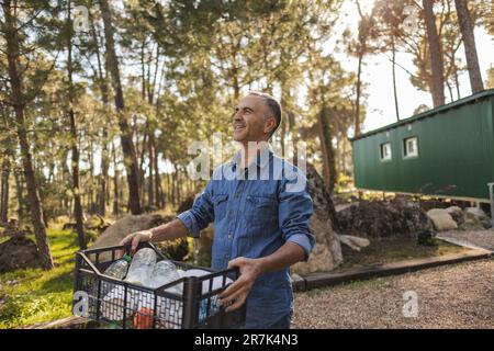 Uomo maturo che trasporta la cassa con i rifiuti separati in giardino Foto Stock