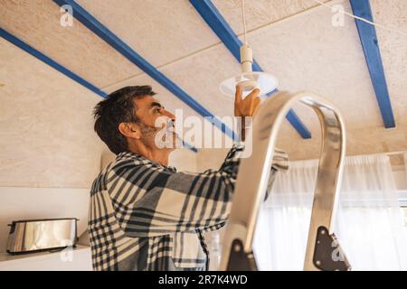 Uomo in piedi sulla scala sostituzione lampadina Foto Stock