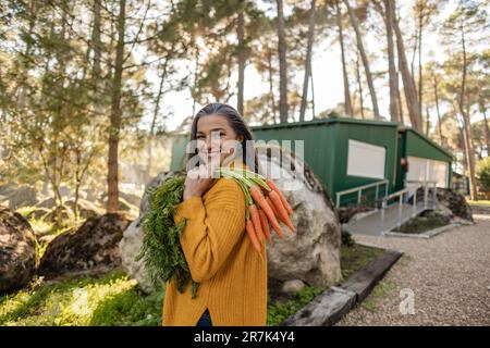 Donna felice che porta mazzo di carote sulla spalla Foto Stock