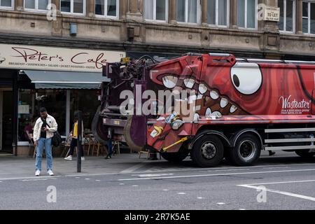 Il grande camion del mangiatore di spreco contrasta con un uomo che guarda il suo telefono sulla strada il 25th maggio 2023 a Londra, Regno Unito. Foto Stock