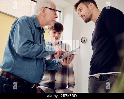 Figlio, padre e nonno che guardano il termostato intelligente sul tablet digitale a casa Foto Stock