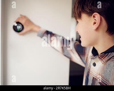 Ragazzo che regola il controllo del termostato intelligente sulla parete a casa Foto Stock