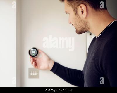 Uomo che regola il controllo del termostato intelligente sulla parete a casa Foto Stock