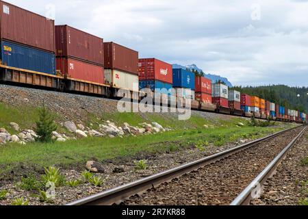 Lago Louise, AB, Canada-Agosto 2022; Vista lungo il argine ferroviario con locomotive canadesi del Pacifico che tirano le automobili con i container Foto Stock