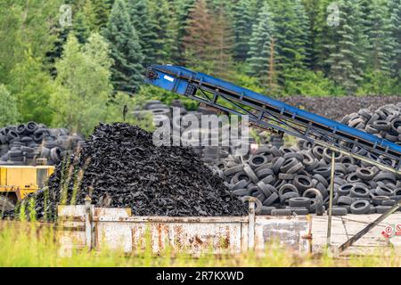 il riciclaggio e la lavorazione dei vecchi pneumatici, la gomma frantumata vanno su un nastro trasportatore a un contenitore Foto Stock