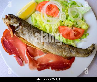 Piatto principale nel ristorante Asturiano, pesce trota intero alla griglia dal fiume di montagna servito con insalata mista fresca e pancetta Foto Stock