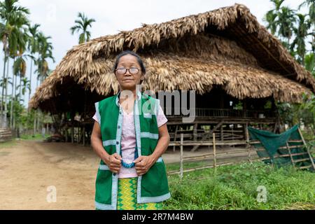 Donna della tribù galo con i suoi abiti tradizionali in posa davanti alla sua casa tradizionale fatta di bambù e palme, assam, india Foto Stock