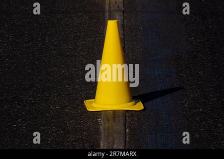 cono stradale giallo sulla linea di demarcazione stradale su asfalto scuro Foto Stock