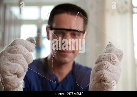 Artigiano in guanti di protezione tenendo due pezzi di vetro nelle mani, tagliò la forma dal vetro Foto Stock