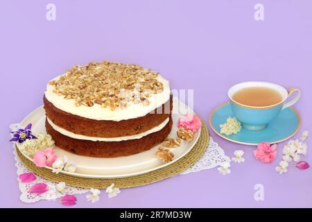 Torta di carote e noci per il tè pomeridiano con tè e fiori estivi su viola. Concetto di cibo fatto in casa per la festa della mamma o di compleanno. Foto Stock