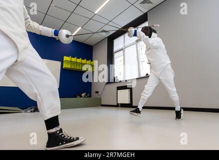 Due atleti di scherma lottano in un'arena sportiva professionale Foto Stock