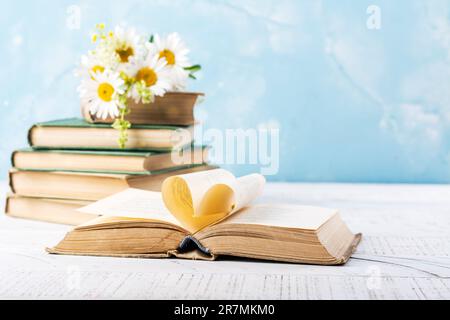 Libro con pagine aperte a forma di cuore e libri impilati sulla scrivania di lettura in biblioteca. Biblioteca nazionale, libri amanti giorno o mese. Di nuovo a scuola o. Foto Stock