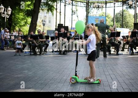 Odessa, Ucraina. 16th giugno, 2023. Una ragazza su uno scooter passa accanto all'Orchestra della Guardia Nazionale d'Ucraina il concerto del Father's Day si è tenuto nel Giardino della Città. La Festa del Padre è una festa annuale in onore dei padri, celebrata in molti paesi. La Giornata del Padre si celebra ogni anno in Ucraina. (Foto di Viacheslav Onyshchenko/SOPA im/Sipa USA) Credit: Sipa USA/Alamy Live News Foto Stock