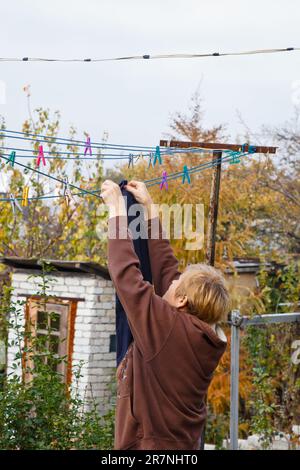 Lavanderia donna appende panno umido pulito su asciugatrice dopo il lavaggio a casa. Faccende domestiche e servizio di pulizia Foto Stock