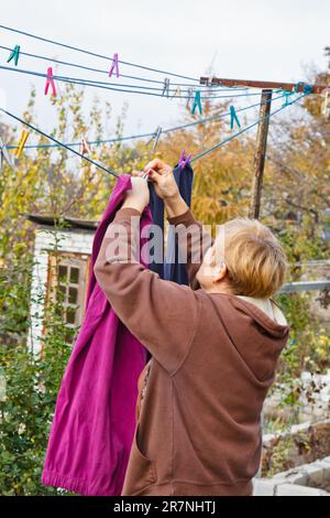 Lavanderia donna appende panno umido pulito su asciugatrice dopo il lavaggio a casa. Faccende domestiche e servizio di pulizia Foto Stock