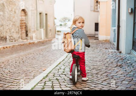 Carina bambina in bicicletta, con zaino, per esplorare la città vecchia europea Foto Stock