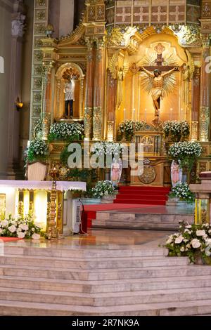 Splendido oro, altare della cattedrale illuminato, con grande statua di Cristo sulla croce, adornato con fiori e gradini di marmo che conducono alla navata. Foto Stock