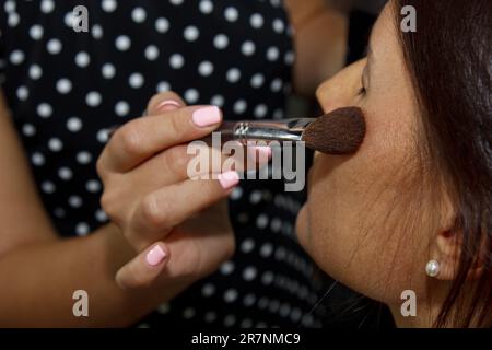 La ragazza dipinge polvere sul viso, completa il make-up occhi di fumo nel salone di bellezza. Cura professionale della pelle Foto Stock