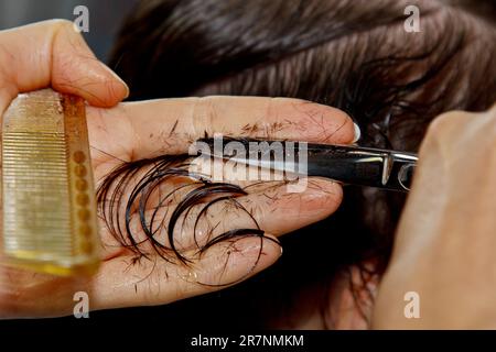 Il closeup di un parrucchiere taglia i capelli marroni bagnati di un cliente in un salone. Il parrucchiere taglia una donna. Vista laterale di una mano che taglia i capelli con le forbici Foto Stock