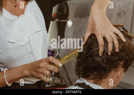 Il closeup di un parrucchiere taglia i capelli marroni bagnati di un cliente in un salone. Il parrucchiere taglia una donna. Vista laterale di una mano che taglia i capelli con le forbici Foto Stock