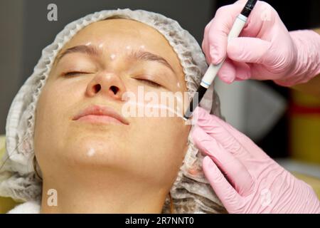 Paziente ragazza attraente con istruzioni sul suo viso per l'operazione di chirurgia plastica. Il chirurgo tocca il viso di una persona. Il concetto di cosmo estetico Foto Stock