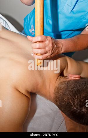 Concetto di benessere. Un massaggiatore professionista offre all'uomo un massaggio tailandese con bastoni di bambù presso la spa. Relax e recupero dopo il lavoro Foto Stock