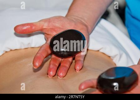 Concetto di benessere. Bel giovane che si rilassa sotto l'effetto stimolante di un tradizionale massaggio con pietre calde in un lussuoso centro termale e benessere. Reg Foto Stock