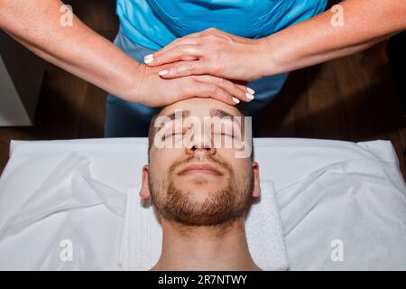 Concetto di benessere. Un massaggiatore professionista offre all'uomo un massaggio tailandese al viso con bastoni speciali in un centro benessere. Relax e recupero dopo il lavoro Foto Stock