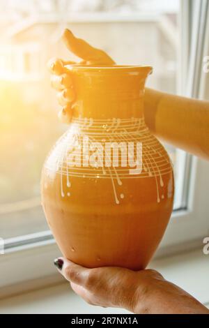 caraffa in terracotta smaltata bianca in mani femminili. primi piatti in ceramica su sfondo sfocato. verticale. Foto Stock