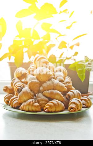 Panini in un piatto pieno di bagel appena sfornati cosparsi di zucchero a velo sul tavolo della cucina. cottura in forno. fase di preparazione dei croissant Foto Stock