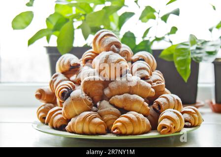 Panini in un piatto pieno di bagel appena sfornati cosparsi di zucchero a velo sul tavolo della cucina. cottura in forno. fase di preparazione dei croissant Foto Stock