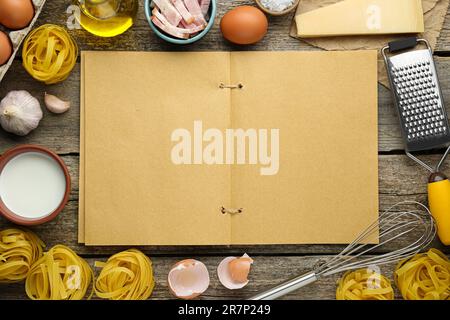 Libro di ricette in bianco circondato da diversi ingredienti su tavolo di legno, piatto. Spazio per il testo Foto Stock