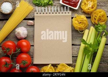 Libro di ricette in bianco circondato da diversi ingredienti su tavolo di legno, piatto. Spazio per il testo Foto Stock