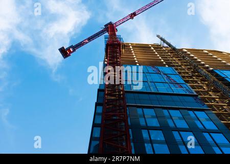 Vista maestosa di una gru rossa alta che opera contro un cielo blu brillante. Ombre e riflessi e una prospettiva impressionante aggiungono un tocco di interesse visivo. Foto Stock