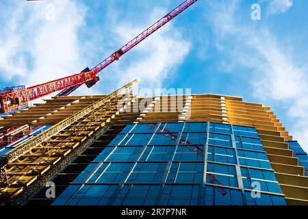 Vista maestosa di una gru rossa alta che opera contro un cielo blu brillante. Ombre e riflessi e una prospettiva impressionante aggiungono un tocco di interesse visivo. Foto Stock