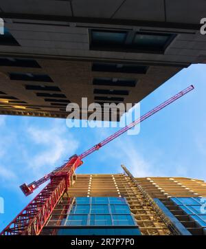 Vista maestosa di una gru rossa alta che opera contro un cielo blu brillante. Ombre e riflessi e una prospettiva impressionante aggiungono un tocco di interesse visivo. Foto Stock