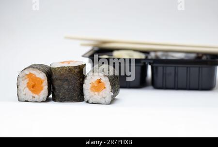 sushi con salmone accanto al confezionamento di alimenti in plastica su sfondo bianco, consegna a domicilio Foto Stock