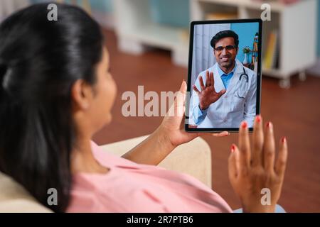 Spalla shot di donna incinta indiana consulenza medico su videochiamata a casa - concetto telemedicina, sanità virtuale e consultazione remota. Foto Stock