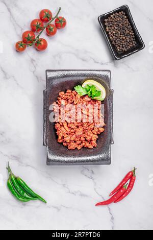 Primo piano di una ciotola di metallo piena di carne macinata, adagiato su un piano di marmo Foto Stock