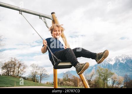 Ragazzo che si diverte a fare altalena nelle alpi svizzere, parco giochi con una splendida vista Foto Stock