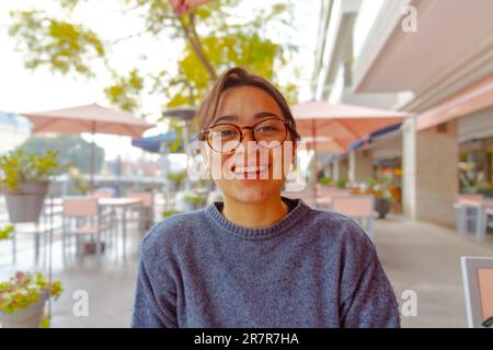 Una giovane donna allegra è seduta in un caffè accogliente durante la stagione invernale, il suo sorriso luminoso che illumina la stanza Foto Stock