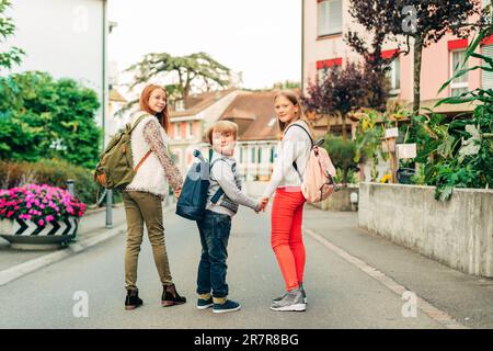 Gruppo di 3 bambini divertenti con zaini, 2 scolaresche e un preschooler, concetto di ritorno a scuola Foto Stock