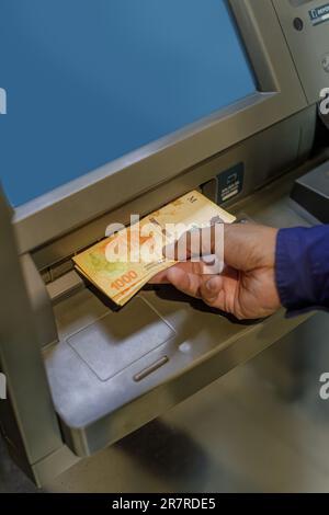 Particolare della mano di un uomo che estrae pesos argentini da un bancomat. Foto Stock